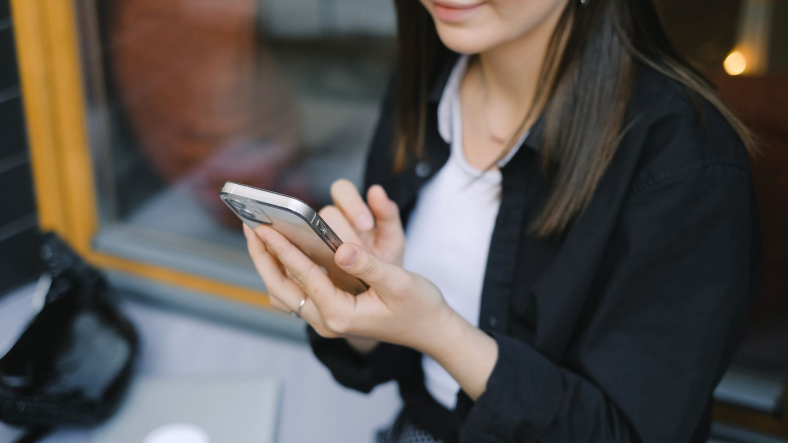 Een vrouw houdt een smartphone vast en kijkt fronsend naar het scherm waarop een vergrendelscherm zichtbaar is, terwijl op de tafel voor haar een opengeslagen notitieboek met handgeschreven aantekeningen ligt, zacht daglicht vanuit een raam