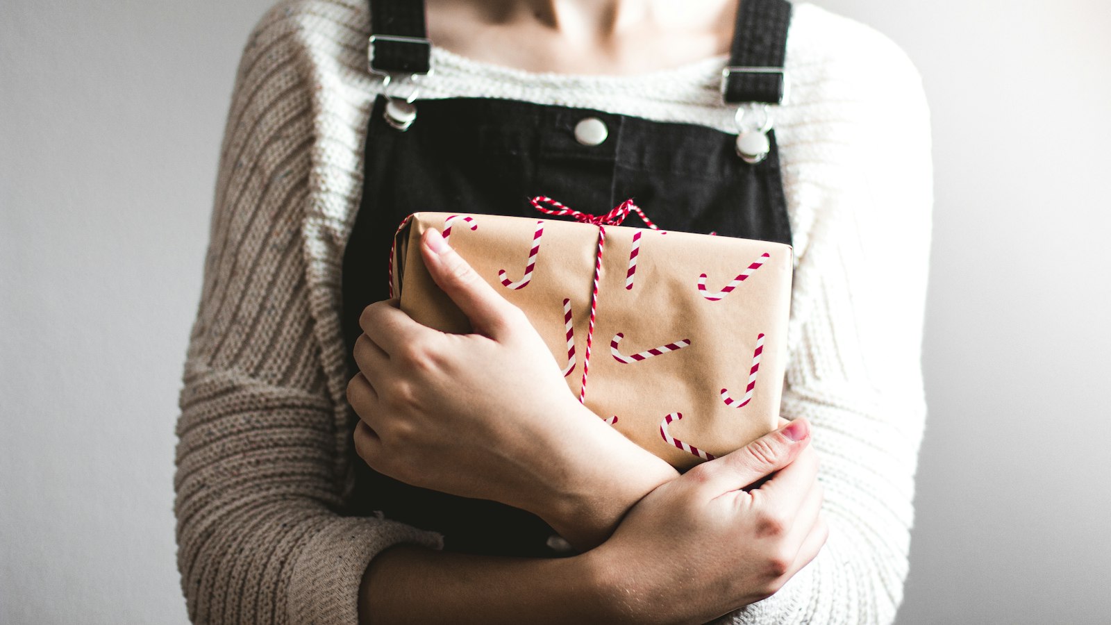 Vrouw in tuinbroek houdt een ingepakt cadeau tegen haar borst.