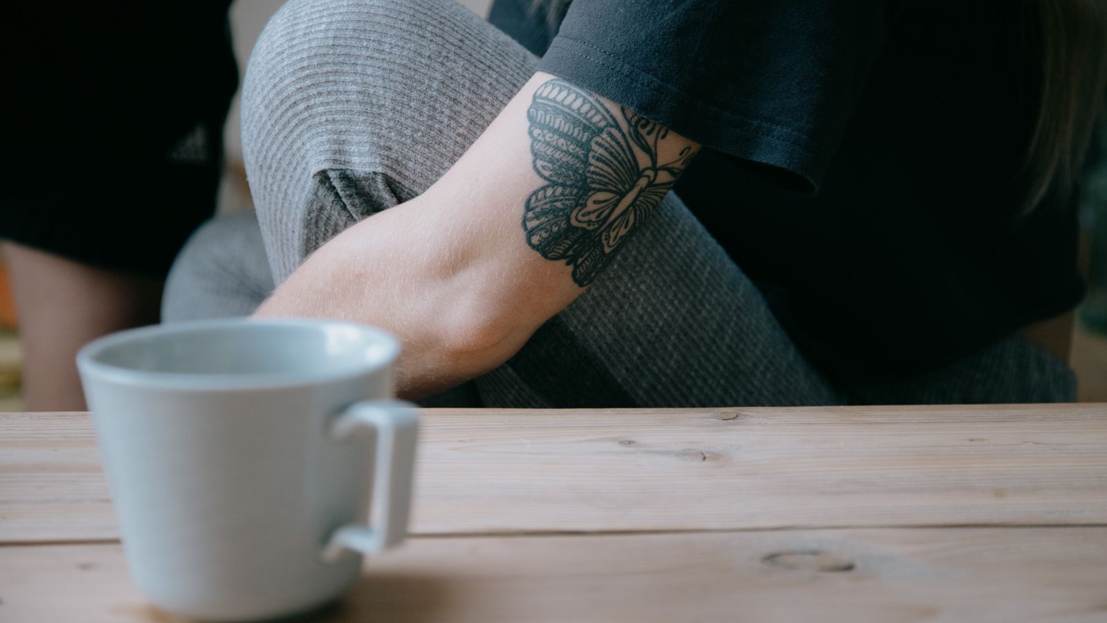 Een volwassen hand schrijft in een geopend notitieboek op een houten tafel, zacht daglicht valt door een raam op de pagina