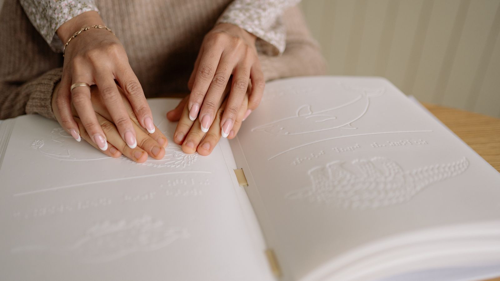 Een volwassen hand en een kleine kinderhand naast een opengeslagen boek op een houten tafel, zacht daglicht vanuit een raam